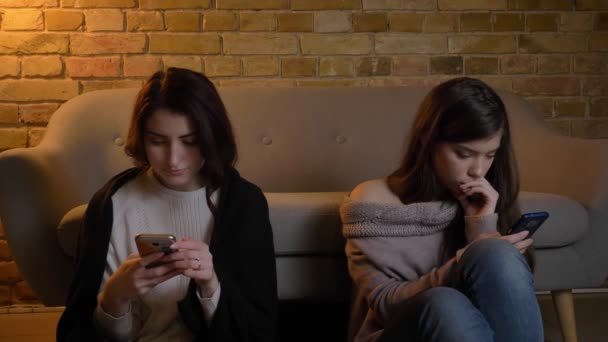 Mladí přátelé Kavkazský žena sedí na podlaze a dívají se do jejich smartphone pozorně v příjemné domácí atmosféře. — Stock video