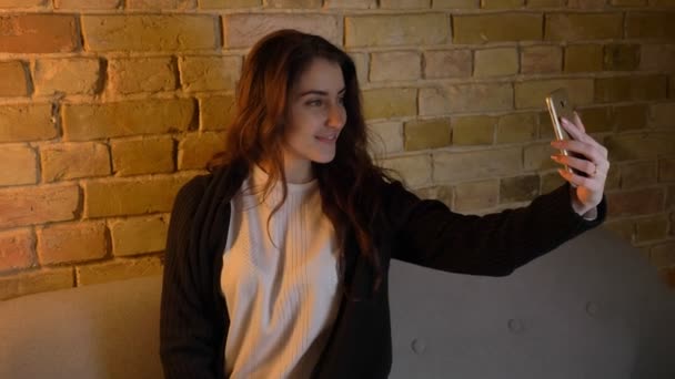 Kaukasische meisje met golvende haren zittend op de Bank en maken selfie-foto vreugdevol op smartphone in huis gezellige. — Stockvideo