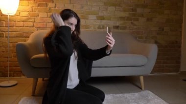 Katta oturan ve selfie-fotoğraf mutlu Smartphone'da rahat ev atmosferde yapma. dalgalı saçlı beyaz genç kız.
