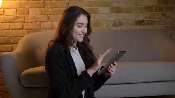 年轻的高加索女孩与波浪形的头发坐在地板上看着平板电脑, 并显示绿色屏幕上的它在舒适的家庭气氛. — 图库视频影像