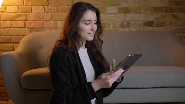 Giovane ragazza caucasica con i capelli ondulati seduto sul pavimento mostrando schermo verde del tablet in un'atmosfera accogliente casa . — Video Stock