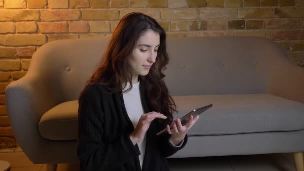 Giovane ragazza caucasica con i capelli ondulati seduto sul pavimento che mostra lo schermo verde del tablet gioiosamente in un'atmosfera accogliente casa . — Video Stock