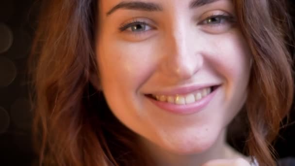 Gros plan portrait de jeune fille caucasienne souriant humblement dans la caméra sur fond de lumières floues . — Video