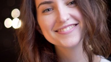 Flirtingly üzerinde kameraya gülümseyen genç beyaz kızın yakın çekim portre ışık arka plan bulanık.
