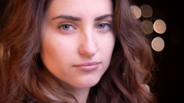 Close-up retrato no perfil de jovem caucasiano menina assistindo sério e flertando em câmera no fundo luzes borradas . — Vídeo de Stock