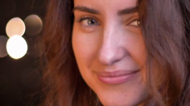 Yakın çekim yarı-portre profil genç beyaz kız kameraya hoş izlerken ışıkları arka plan bulanık.