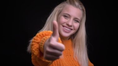 Closeup vur genç oldukça beyaz kadın gösteren başparmak ise kameraya bakıyor ve arka plan üzerinde siyah izole ile gülümseyen