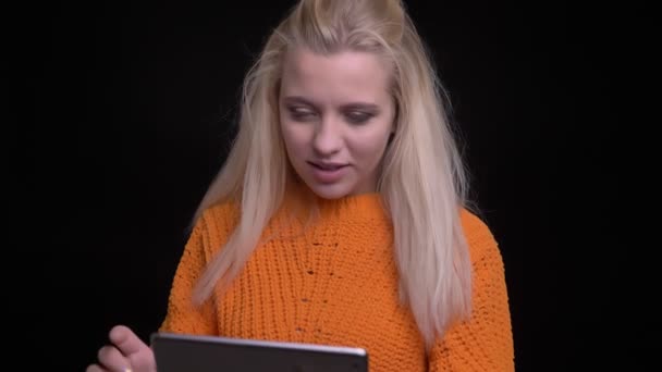 Primer plano de brote de joven atractiva hembra caucásica utilizando la tableta que muestra la pantalla azul a la cámara y sonriendo alegremente — Vídeo de stock