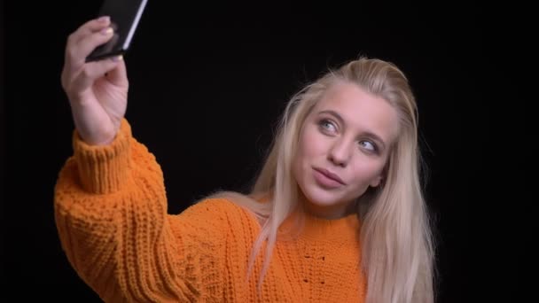 Closeup shoot of young pretty caucasian female taking selfies on the phone and posing in front of the camera smiling — Stock Video