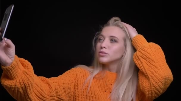 Close-up opnamen van jonge mooie Kaukasische vrouwelijke nemen selfies op de telefoon met geïsoleerd op zwarte achtergrond — Stockvideo