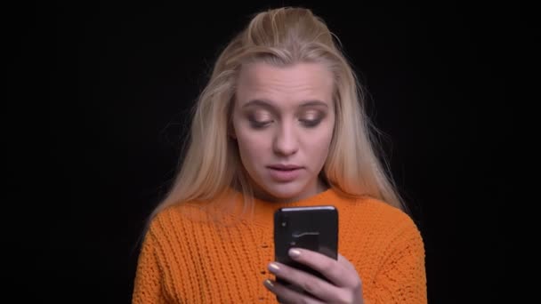 Nahaufnahme Porträt einer jungen hübschen kaukasischen Frau, die am Telefon surft und dann lächelnd in die Kamera schaut — Stockvideo
