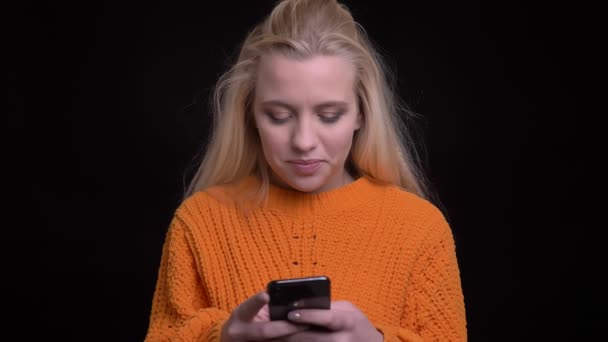 Close-up tiro de jovem muito caucasiano feminino mensagens de texto no telefone e sorrindo alegremente na frente da câmera — Vídeo de Stock