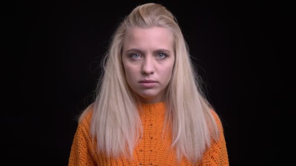 Gros plan pousse de jeune femme caucasienne élégante avec de longs cheveux blonds regardant directement la caméra avec un arrière-plan isolé sur noir — Video