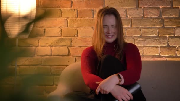 Nahaufnahme einer jungen, gut gelaunten kaukasischen Frau, die auf der Couch lächelnd und lachend eine Komödie im Fernsehen anschaut — Stockvideo