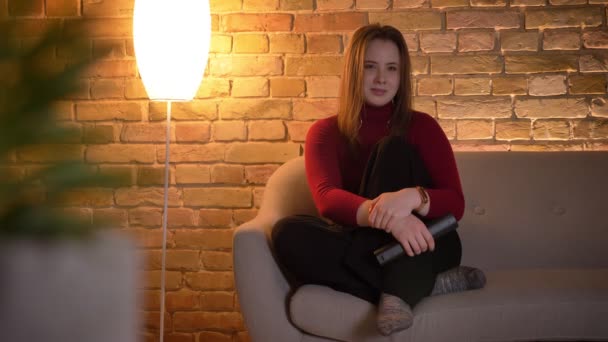 Closeup schieten van jonge vrolijke Kaukasische vrouw kijken naar een komedie op Tv glimlachen en lachen in een gezellig appartement — Stockvideo