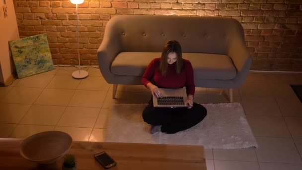 Closeup top shoot of young pretty caucasian female using the laptop sitting on the floor at cozy home indoors — Stock Video