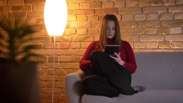 Close-up opnamen van jonge mooie Kaukasische vrouw met behulp van de tablet zittend op de Bank binnenshuis — Stockvideo