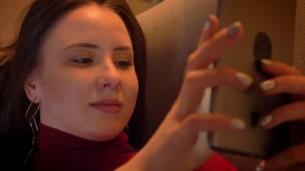 Closeup shoot of young charming caucasian female texting on the tablet and smiling while lying on the sofa in a cozy apartment indoors — Stock Video