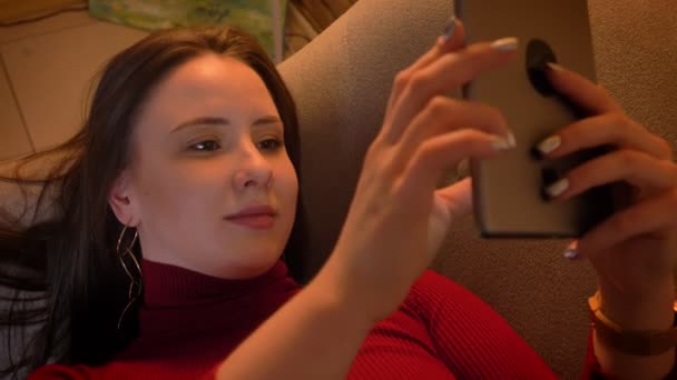 Closeup shoot of young pretty caucasian female typing on the tablet while lying on the couch indoors — Stock Video