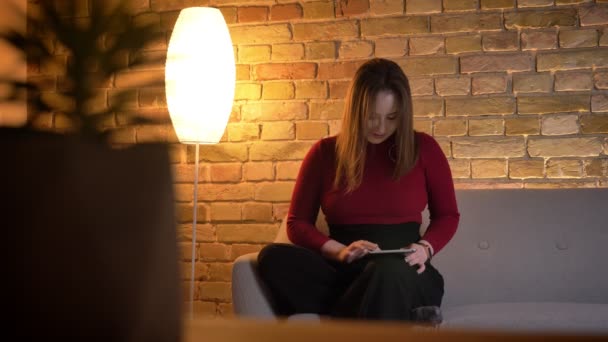 Closeup πυροβολούν νέοι αρκετά καυκάσιος γυναίκα πληκτρολογώντας στο tablet ενώ κάθεστε στον καναπέ, σε εσωτερικούς χώρους — Αρχείο Βίντεο