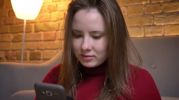 Nahaufnahme Porträt einer jungen charmanten kaukasischen Frau, die das Telefon benutzt, dann in die Kamera schaut und glücklich lacht — Stockvideo