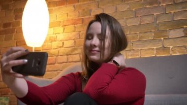 Selfies telefon gülümseyen üzerinde yapma ve rahat bir daire içinde soğutma poz genç oldukça beyaz kadın portre çekimleri