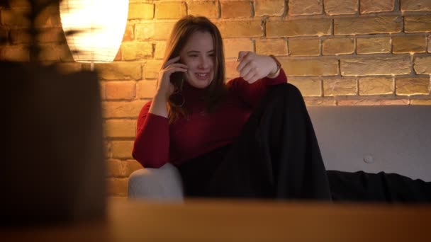 Gros plan shoot de jeune jolie femme caucasienne ayant une conversation joyeuse au téléphone dans un appartement confortable à l'intérieur — Video