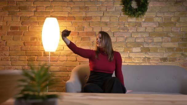 Närbild-shoot av unga ganska kaukasisk kvinna att ta selfies på telefonen och leende sitter i soffan — Stockvideo