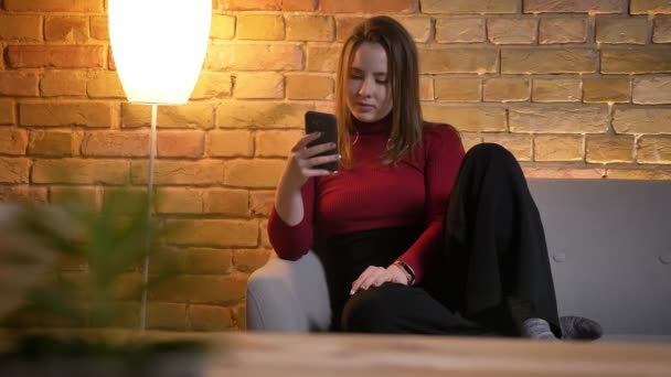 Gros plan shoot de jeune jolie caucasienne femelle en utilisant le téléphone tout en étant assis sur le canapé — Video