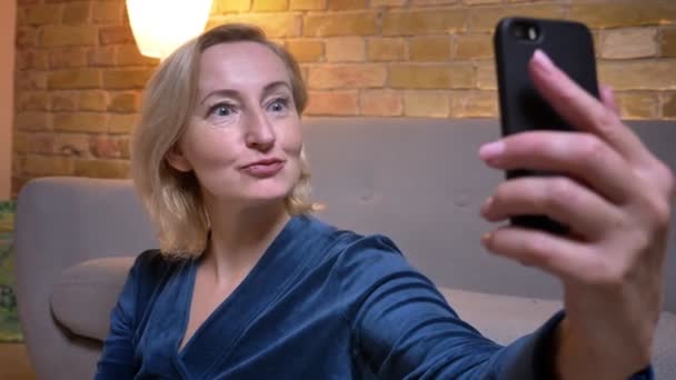 Κοντινό γύρισμα της ατερής καυκάσιας γυναίκας που παίρνει selfie σε άλλο τηλέφωνο και κάνοντας αστείες εκφράσεις του προσώπου που ποζάρουν μπροστά από την κάμερα — Αρχείο Βίντεο
