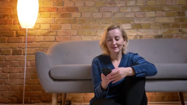 Closeup shoot of eldery caucasian female texting on the phone while sitting on the floor in a cozy apartment — Stock Video