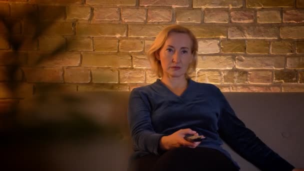 Střevný zastřelením eldery kavkazské ženy, která pozoruje show v televizi pozorně se zvědavé tváře, sedící na pohovce uvnitř — Stock video