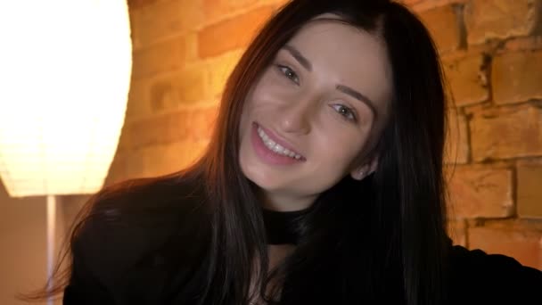 Close-up portret van jonge brunette Kaukasisch meisje glimlachen bescheiden in de camera in huiselijke sfeer. — Stockvideo