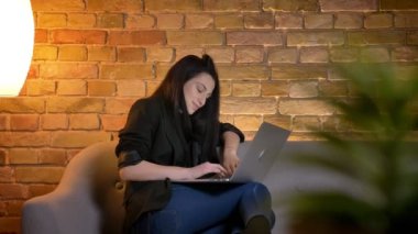 Ev atmosferinde memnuniyeti ile Laptop içine izlerken kanepede genç esmer beyaz kız profilinde portre.