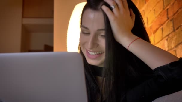 Primer plano retrato de la joven morena caucásica chica en el sofá viendo en el ordenador portátil felizmente en el ambiente de casa . — Vídeos de Stock