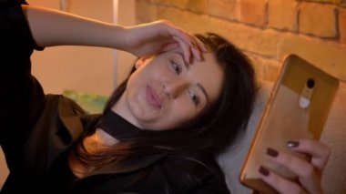 Genç esmer beyaz kız kanepede oturan ve ev atmosferinde selfie-fotoğraf yapma yakın yukarı portre.