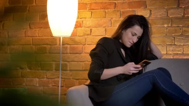 Portrait de jeune fille caucasienne brune assise sur un canapé et faisant des selfie-photos sérieusement dans l'atmosphère de la maison . — Video