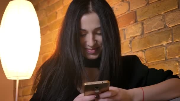Portrait de jeune fille caucasienne brune tapant sur smartphone sourit volontiers dans la caméra dans l'atmosphère de la maison . — Video