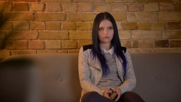 Nahaufnahme einer jungen hübschen kaukasischen Frau, die zu Hause fernsieht, sensibel ist und weint, wenn sie drinnen auf der Couch sitzt — Stockvideo