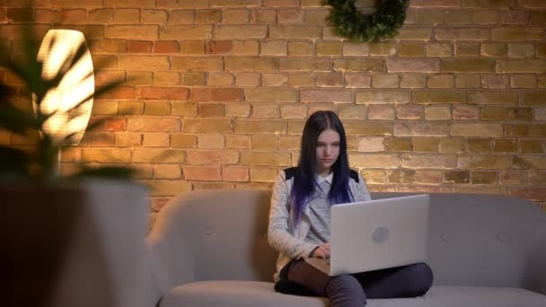 Primo piano ripresa di giovane bella femmina caucasica guardando un video sul computer portatile e sorridendo mentre seduto sul divano al chiuso — Video Stock