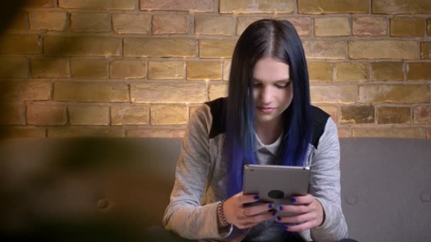 Närbild skjuta av unga vackra kaukasiska kvinnlig skriva på tabletten medan du sitter på soffan i en mysig lägenhet inomhus — Stockvideo
