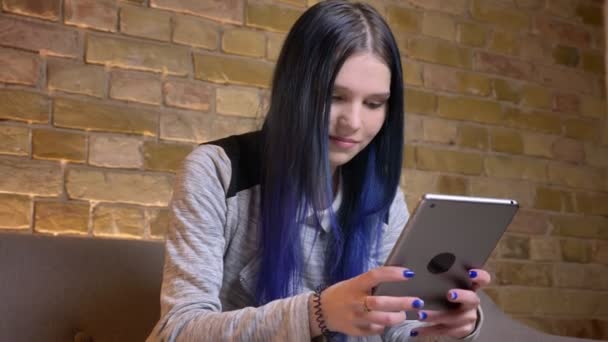 Tiro close-up de jovem muito caucasiano hipster fêmea com texting cabelo tingido no tablet e sorrindo em um aconchegante apartamento dentro de casa — Vídeo de Stock