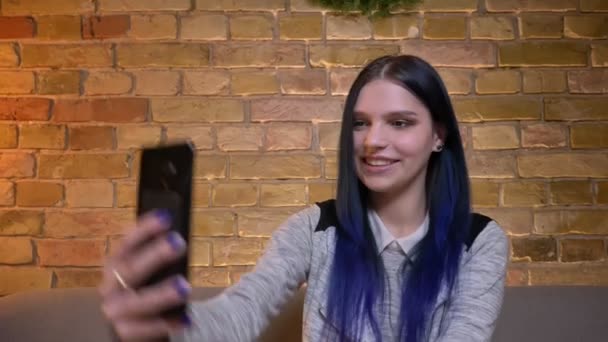 Nahaufnahme einer jungen hübschen kaukasischen Frau, die ein lockeres Gespräch per Videotelefon führt und glücklich lächelt, während sie auf der Couch in einer gemütlichen Wohnung sitzt — Stockvideo