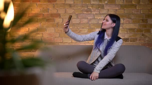 Closeup portrait of young attractive caucasian female having a video call on the phone cheerfully smiling while sitting on the couch at cozy home indoors — Stock Video