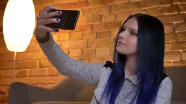 Primo piano di ripresa della giovane ragazza adolescente hipster caucasica bella prendendo selfie al telefono e sorridendo in un accogliente appartamento con interni moderni — Video Stock