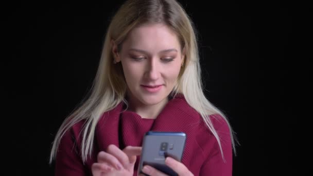 Närbild skjuta av unga vackra kaukasiska hona med hjälp av telefonen och tittar rakt på kameran — Stockvideo