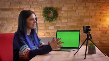 Closeup ateş genç çekici beyaz kadın blogger video fotoğraf makinesi üzerinde akış ve dizüstü bilgisayar ile yeşil ekran kullanarak aboneleri için konuşuyor canlı