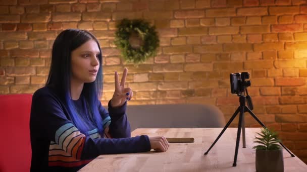 Gros plan shoot of young attractive hipster female video blogger talking while streaming live on the camera gesturing indoors in a coszy apartment — Video