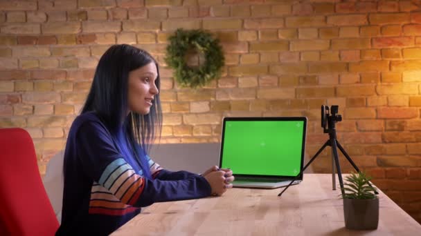 Close-up opnamen van jonge aantrekkelijke trendy vrouwelijke video blogger live streaming op de camera met behulp van de laptop met groene chroma scherm — Stockvideo