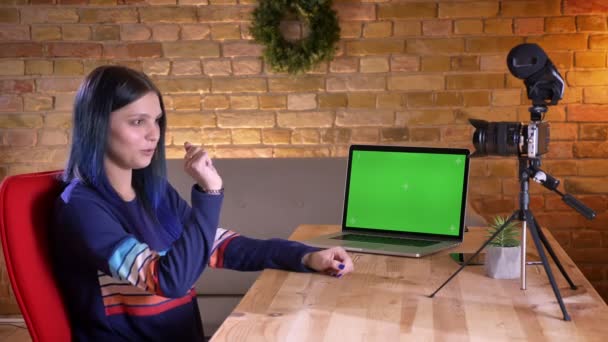 Крупный план портрета молодой привлекательной кавказской блоггерки, транслирующей видео на камеру и обсуждающей зеленый экран ноутбука — стоковое видео